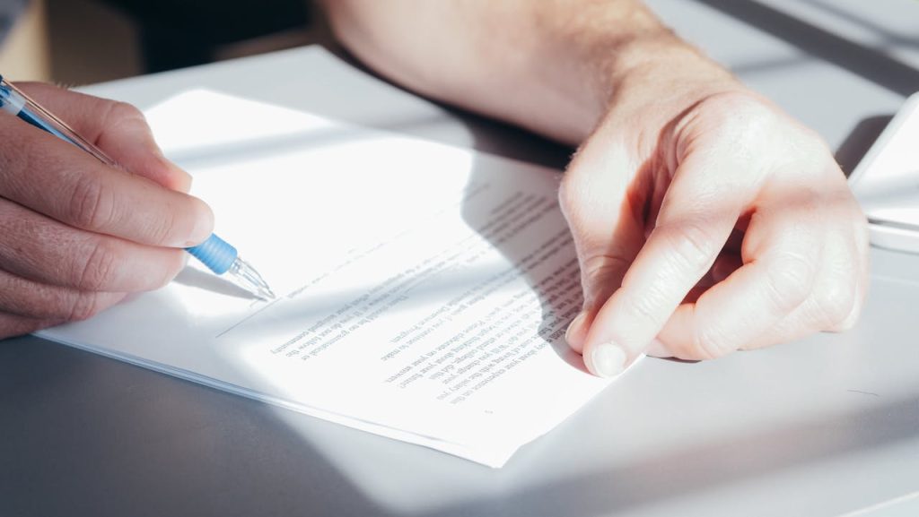 a-person-signing-a-document-7054502 Hands signing a contract with a blue pen, close-up view.